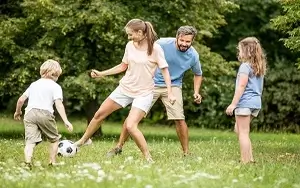 Elternpaar und ihre 2 Kinder spielen im Garten Fußball